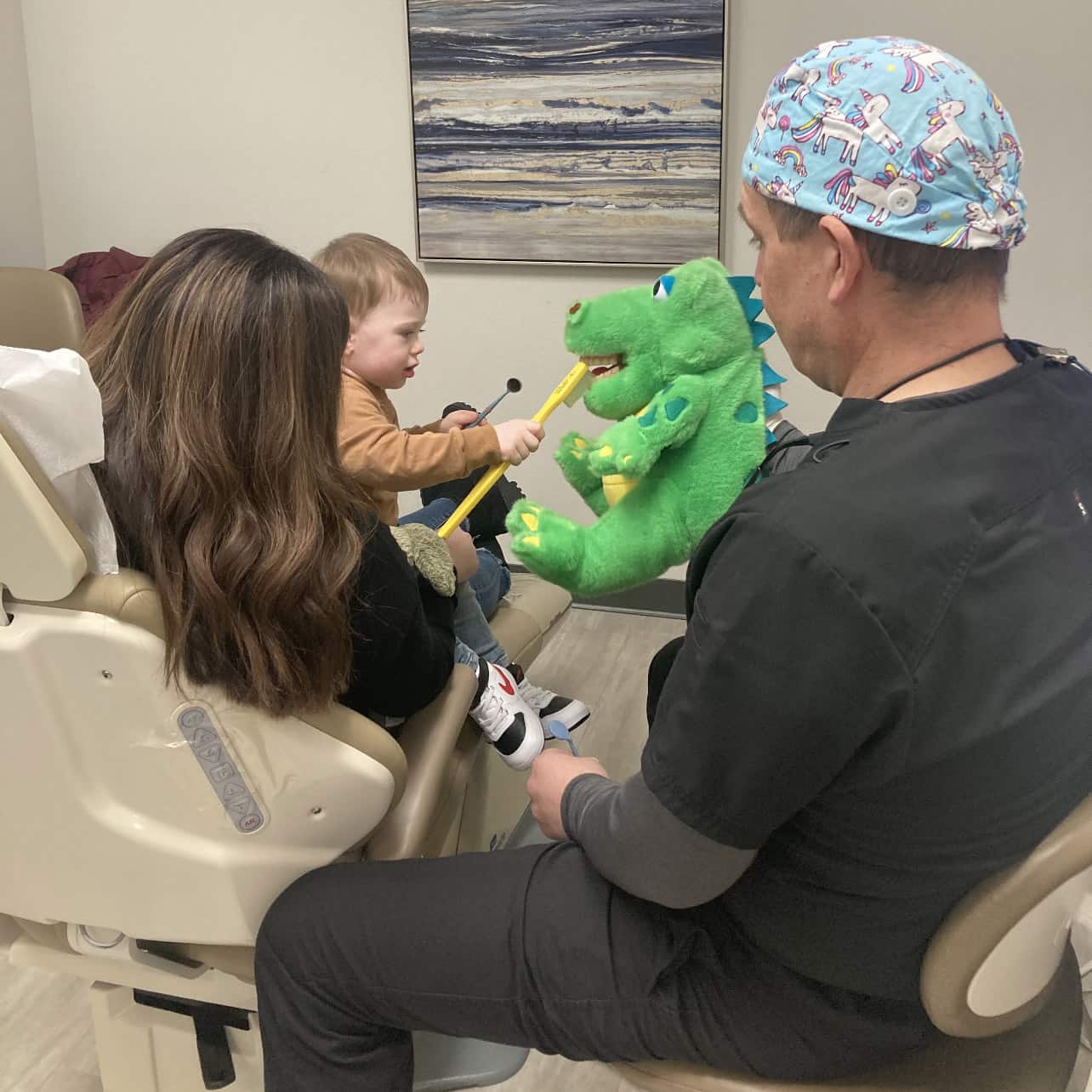 Family dentist sitting with mother and child and using a dinosaur to teach the child about healthy brushing.